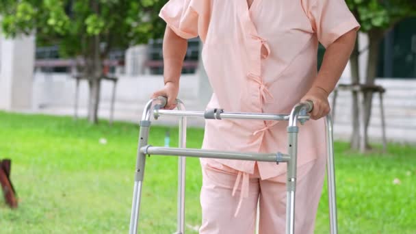 Iloinen vanha aasialainen nainen käyttää kävelijää ja kävelee sairaalaan onnettomuuden jälkeen. Onnellisen eläkkeelle siirtymisen käsite Hoitaja ja säästöt ja vanhempi sairausvakuutus - Materiaali, video