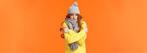 Sad cute redhead girl feeling discomfort, shaking from freezing cold, embracing own body get warm, frowning and grimacing unhappy, sulking, standing outside low temprature in hat and scarf. - 写真・画像