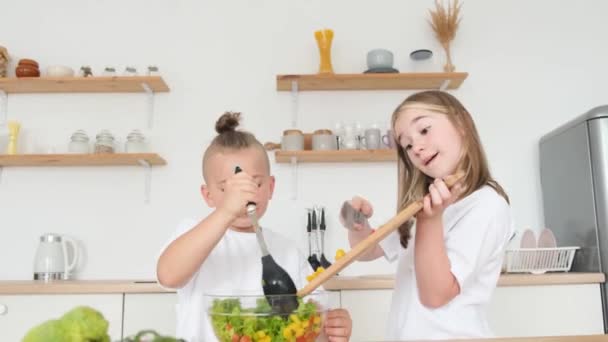 Roztomilý chlapec a dívka připravuje čerstvý zeleninový salát v moderní kuchyni. Děti doma. Zdravé stravování - Záběry, video