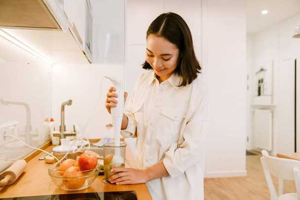 Young cute beautiful smiling asian girl cooking smoothie in cozy kitchen at home - Foto, Imagem
