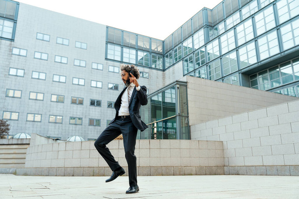 Young entrepreneur business man listening to music and dancing outside the office. Concept about freedom and success in business - Фото, изображение