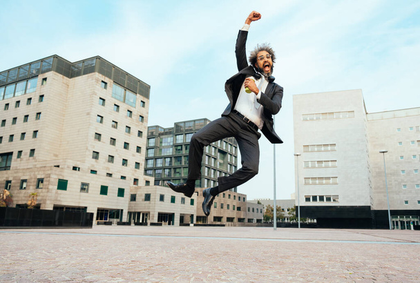 Jeune entrepreneur sautant et dansant pour célébrer sa journée réussie au travail. Concept de liberté et d'insouciance dans la carrière professionnelle - Photo, image
