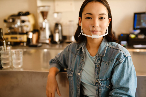 Young asian waitress woman in face mask smiling while working at cafe - Foto, imagen