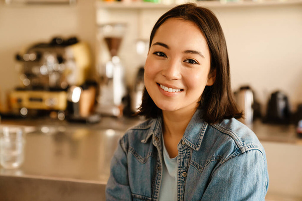 Young asian woman wearing denim shirt smiling and looking at camera at cafe - Foto, afbeelding