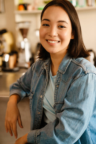 Young asian woman wearing denim shirt smiling and looking at camera at cafe - Fotografie, Obrázek