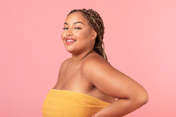Portrait of obese african american woman wrapped in towel smiling at camera, posing over pink studio background. Beauty routine and wellness concept - Фото, изображение