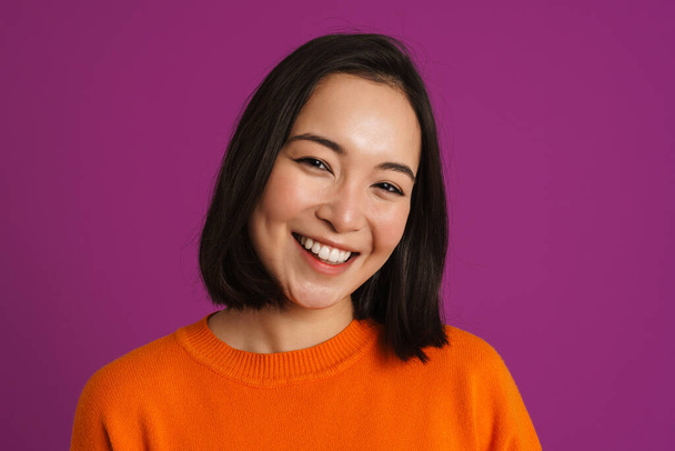 Young asian woman smiling and looking at camera isolated over purple background - Foto, Imagen