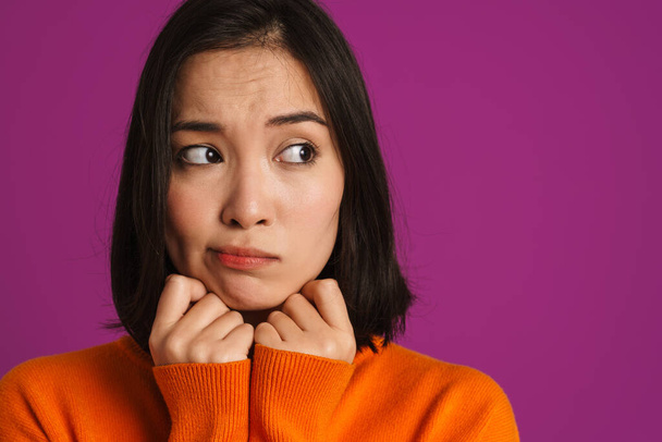Young asian woman wearing sweater frowning and looking aside isolated over purple background - Zdjęcie, obraz