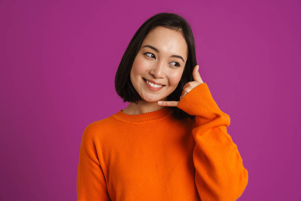 Young asian woman smiling and making handset gesture isolated over purple background - Zdjęcie, obraz