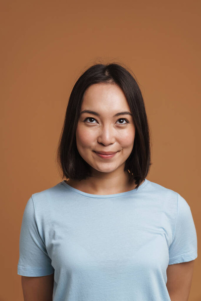 Jeune femme asiatique portant t-shirt souriant et regardant vers le haut isolé sur fond beige - Photo, image