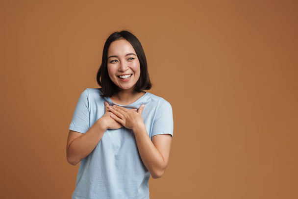 Young asian woman laughing and holding hands on her chest isolated over beige background - Foto, Imagem