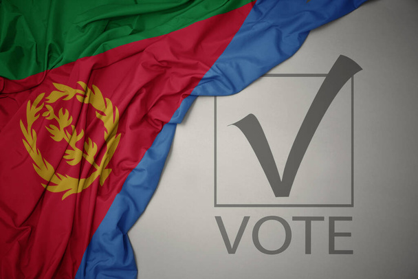 ondeando colorida bandera nacional de eritrea sobre un fondo gris con voto de texto. concepto de elección. Ilustración 3D - Foto, imagen