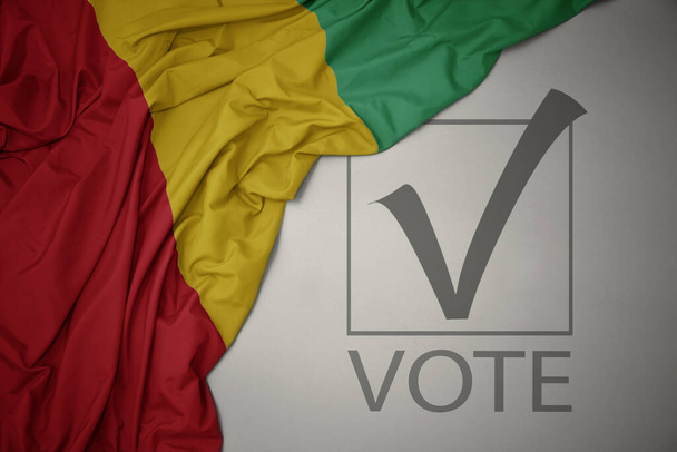 agitant drapeau national coloré de la Guinée sur un fond gris avec vote de texte. concept électoral. Illustration 3D - Photo, image