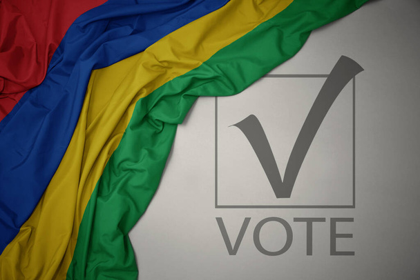 ondeando colorida bandera nacional de Mauricio sobre un fondo gris con voto de texto. concepto de elección. Ilustración 3D - Foto, imagen
