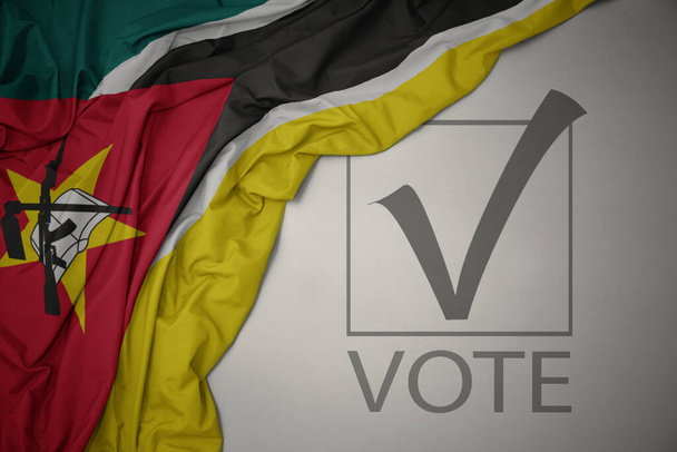 ondeando colorida bandera nacional de Mozambique sobre un fondo gris con voto de texto. concepto de elección. Ilustración 3D - Foto, imagen