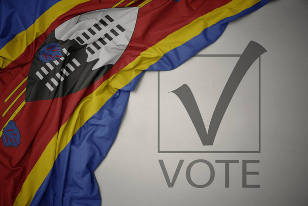 ondeando colorida bandera nacional de eswatini sobre un fondo gris con voto de texto. concepto de elección. Ilustración 3D - Foto, imagen