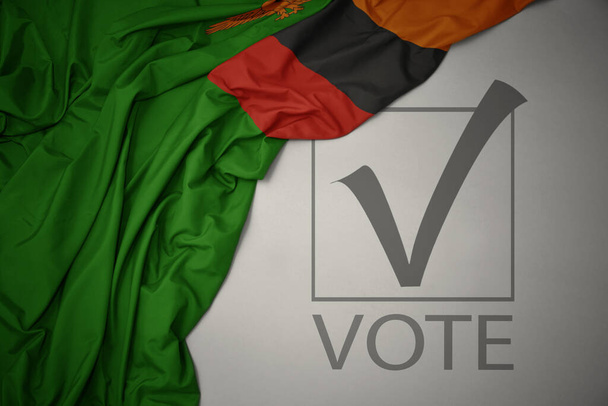 zwaaiende kleurrijke nationale vlag van Zambia op een grijze achtergrond met tekst stemmen. verkiezingsconcept. 3D illustratie - Foto, afbeelding
