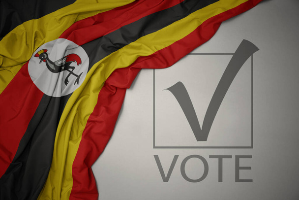 ondeando colorida bandera nacional de uganda sobre un fondo gris con voto de texto. concepto de elección. Ilustración 3D - Foto, imagen