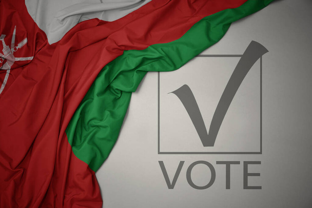 ondeando colorida bandera nacional de Oman sobre un fondo gris con voto de texto. concepto de elección. Ilustración 3D - Foto, imagen