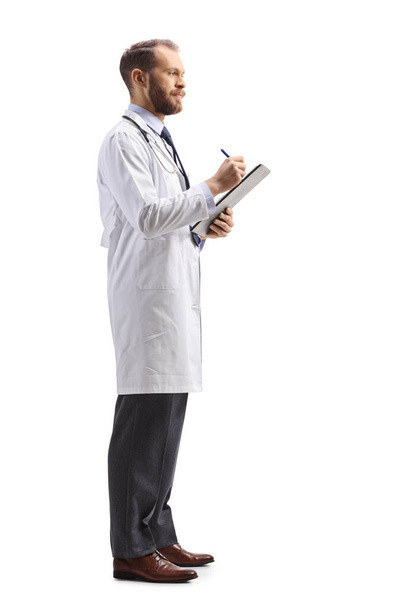Full length profile shot of a male physician standing and writing a document isolated on white background  - Photo, image