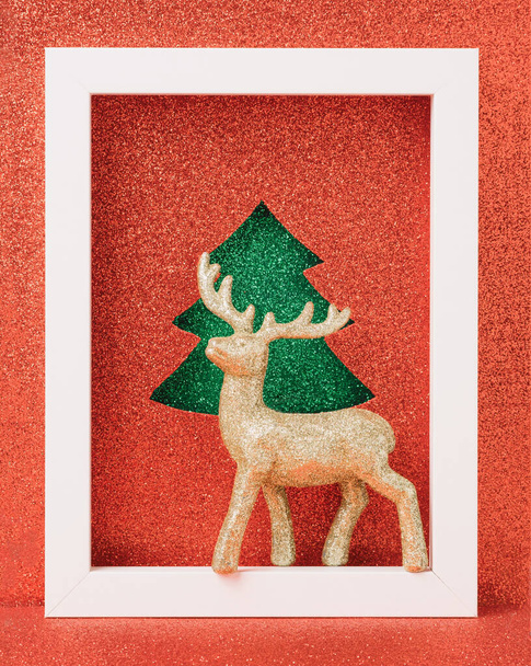 Golden reindeer ornament on a white wooden frame. Christmas red glitter background. Holiday spirit concept. - Photo, Image