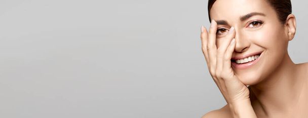 Schoonheid en huidverzorging concept. glimlachende natuurlijke jonge vrouw gezicht met naakt make-up op een vlekkeloze huid geïsoleerd op grijze achtergrond met kopieerruimte - Foto, afbeelding