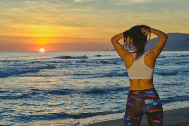 Vue arrière d'un ajustement caucasien et femme sportive sensuelle regardant le coucher de soleil de la plage - Photo, image