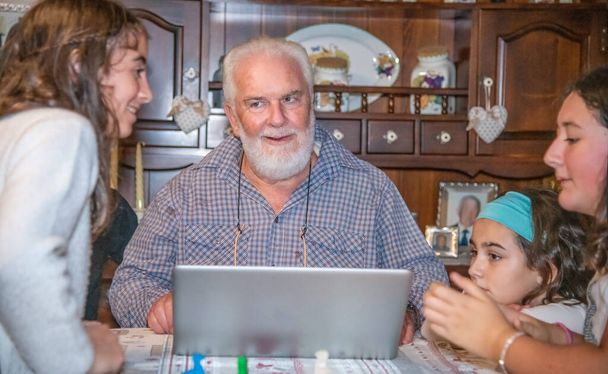 Grandfather using laptop indoor with his grandchildren - Фото, изображение