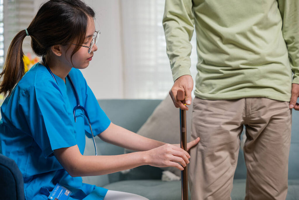 Azjatycki lekarz pytający i wyjaśniający starszego mężczyznę o objaw bólu laską, młoda pielęgniarka sprawdzająca kolano i nogę po operacji seniora starszego mężczyzny cierpiącego na ból kolana - Zdjęcie, obraz