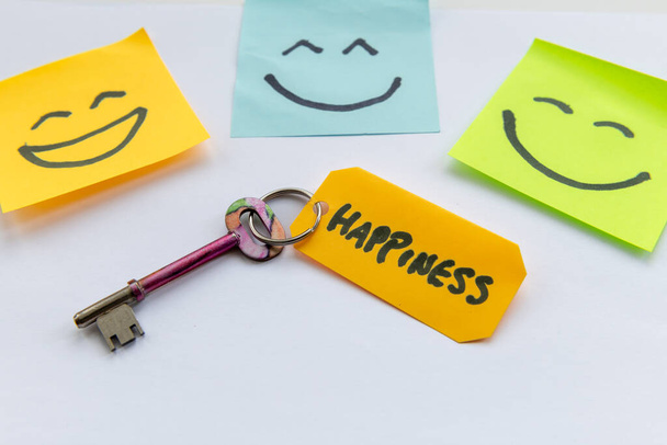 Una clave para el concepto de felicidad con una llave y caras felices dibujadas a mano aisladas en un fondo blanco. - Foto, imagen