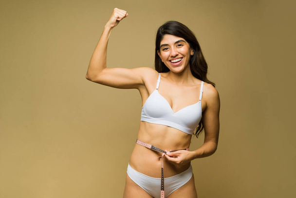 Vrolijke opgewonden vrouw in ondergoed doet een biceps krullen en ziet er sterk uit met haar atletische lichaam tijdens het eten - Foto, afbeelding