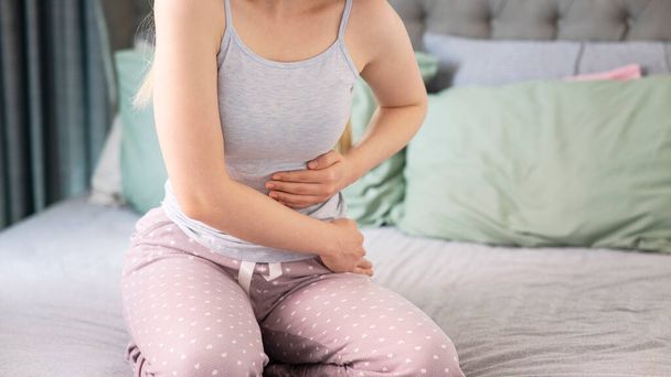 Mujer joven con dolor acostada en la cama en casa. dolor de estómago - Foto, Imagen