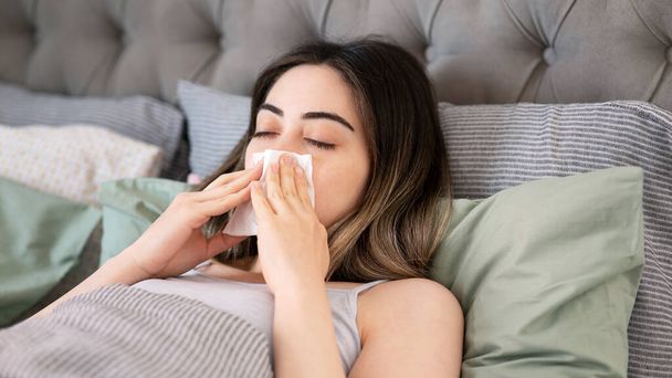 νεαρή γυναίκα άρρωστος που φυσούν τη μύτη της ενώ στο κρεβάτι - Φωτογραφία, εικόνα