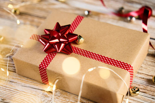 Powyższy widok świąteczne pudełko zapakowane w papier rzemieślniczy z świątecznych wstążek i łuku. Prezent na święta Bożego Narodzenia na drewnianym tle z bokeh światła - Zdjęcie, obraz