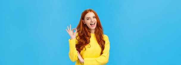 Waist-up shot carefree cheerful and friendly redhead gorgeous female freelancer finished IT school and showing okay gesture, no problem sign, smiling unbothered, assure all good, blue background. - Фото, изображение