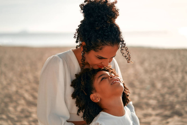 Афро-американка мама со своей милой дочерью с афро кудряшками стоит обнимая на берегу моря на рассвете в свои выходные. - Фото, изображение