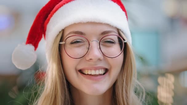 Közelkép portré vicces mosolygós fogas nevetés boldog kaukázusi nő lány hölgy visel Mikulás karácsonyi kalap és szemüveg nézi kamera mosoly nevetés fejlövés női arc Újévi ünneplés - Felvétel, videó