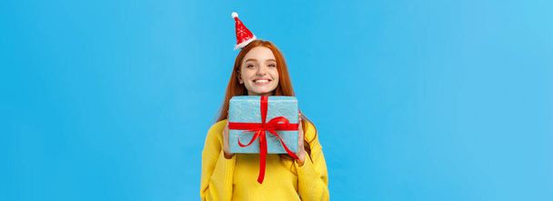 Захоплена і щаслива мила руда дівчина насолоджується святкуванням Різдва, таємна подія Санти як отримує багато подарунків, тримає подарунок, хвалиться синім загорнутим новорічним подарунком, радісно посміхається
. - Фото, зображення