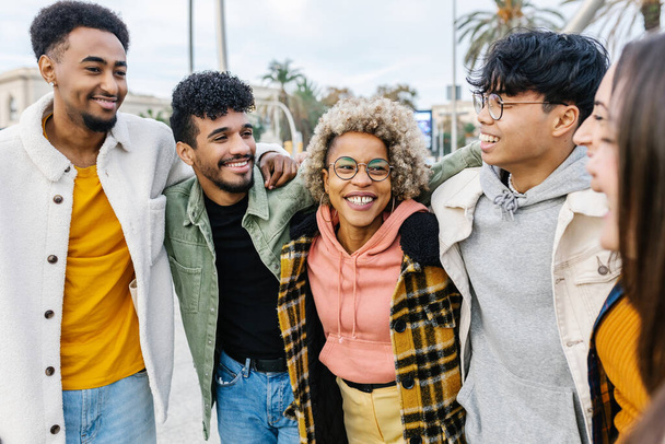 Multiracial young friends having fun in city street. United millennial people hugging each other standing together outdoors. Multi-ethnic friendship and youth concept - Photo, Image