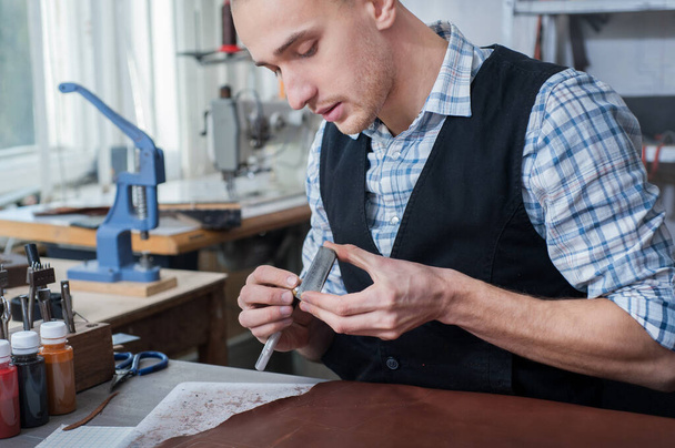 un artesano agudiza el borde de una herramienta de cuero en un taller - Foto, imagen