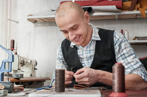 Produção de produtos de couro, close-up do processo. o mestre sorri no processo de costura manual do produto. Fios para costura, costura de artigos de couro. - Foto, Imagem