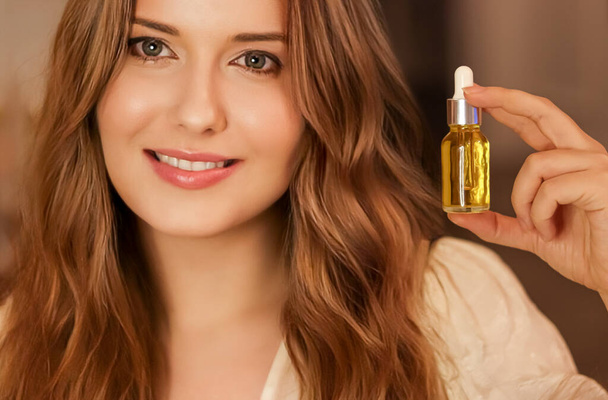 Beautiful woman holding organic oil serum bottle and smiling, evening beauty and skincare routine. - Photo, Image