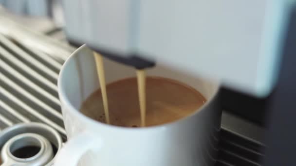 Кофеварка делает эспрессо и ристретто утром. Горячий ароматический кофе по утрам. Черный эспрессо наливается в белую чашку - Кадры, видео