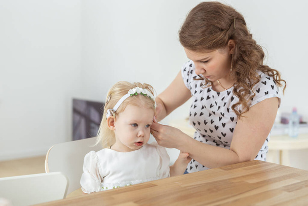 Mother helps her deaf baby daughter putting hearing aid in little girls ear indoors - cochlear implant and innovative medical technologies - Valokuva, kuva