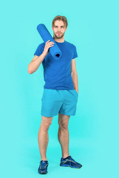 sport man with yoga mat standing in studio. photo of sport man with yoga mat. sport man with yoga mat wearing sportswear. sport man with yoga mat isolated on blue background. - Fotoğraf, Görsel