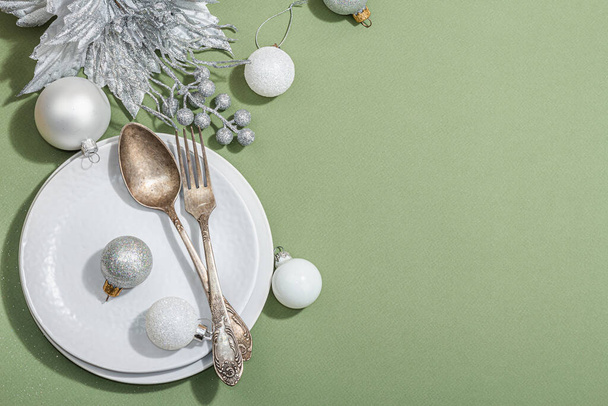 Joulupöytä, jossa tyhjät keraamiset laatat, perinteiset tarvikkeet trendikkäällä Savannah Green väritaustalla. Juhlava uudenvuoden ruokailuvälineet, kova valo, tumma varjo, tasainen lay, ylhäältä - Valokuva, kuva