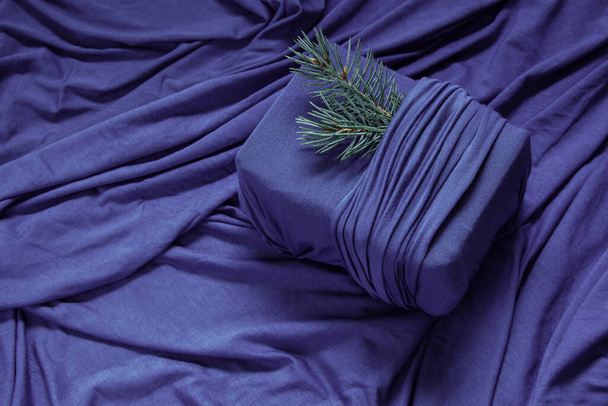 トレンディゼロ廃棄物ギフト包装。持続可能なデザインコンセプト。生地の折り目を持つ紫色の背景に生地に存在するクリスマス - 写真・画像