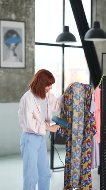 Belle femme au foyer aux cheveux roux repasse les vêtements avec un vapeur - Séquence, vidéo