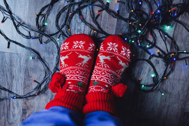 Luces de Navidad enredadas en el suelo a los pies con calcetines rojos de Navidad. Coros de invierno, limpieza antes y después de las vacaciones, gastos de electricidad y concepto de presupuesto para el hogar - Foto, imagen