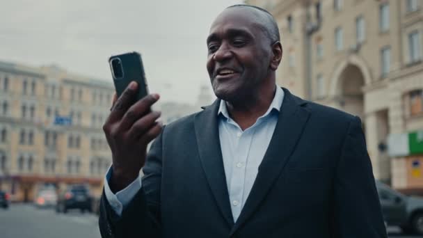 Африканский взрослый мужчина среднего возраста этнический мужчина консультант работодатель бизнесмен предприниматель на городской улице на открытом воздухе говорить мобильный телефон камера разговор смартфон видео-конференция видеозвонок виртуальный чат - Кадры, видео